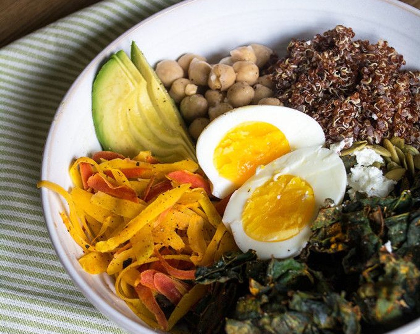 step 10 In two bowls, add cooked quinoa, baked kale chips, GOYA® Chick Peas (1/2 cup), shaved carrots, Avocado (1/2), Goat Cheese (2 Tbsp) and Pepitas (2 Tbsp) then top with soft boiled egg and sprinkle with salt and pepper if desired.